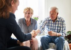 Financial advisor shaking hands with senior man in living room. Retired couple in meeting with a female financial advisor at home.