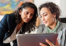 Two business women looking at a tablet computer, discussing a topic.
