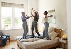 Full length of cheerful young women dancing on bed enjoying slumber party at home